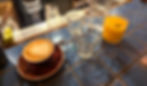 One cup of flat white coffee in a burgundy mug and saucer with a creative milk art in the coffee. Alongside this is a regular sized orange juice in a rocks glass and two empty glasses for water at The Breakfast Club's bar.