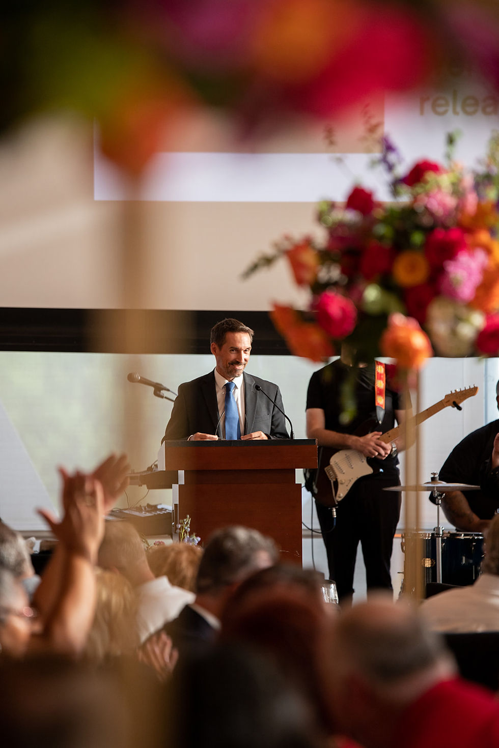 Official speaker on stage while crowd claps at event. By Arkansas Event Photographer Kalen Kemp