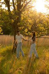 couple walking in field in front of a tree at golden hour. Woman holding baby bump.