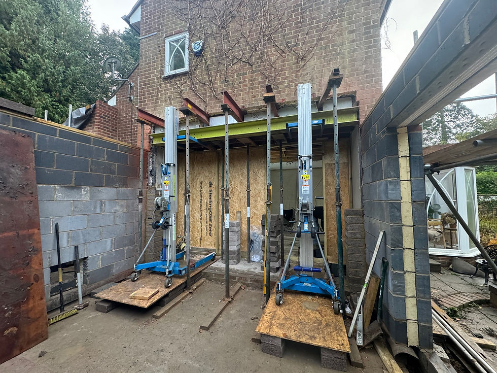 Construction site with a brick building, scaffolding, and jacks in place. There's exposed plywood and brick walls, with equipment and tools around.