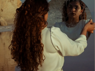 woman in a white long sleeve dress looking in a mirror outside in daylight