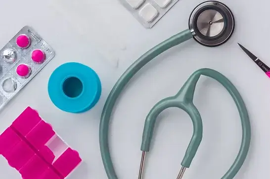 Stethoscope, pills, pink pill organizer, blue tape on white background. Medical theme with vibrant colors, no visible text.