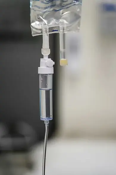 IV drip with clear fluid hangs against a blurred hospital background. The setting feels clinical and sterile.