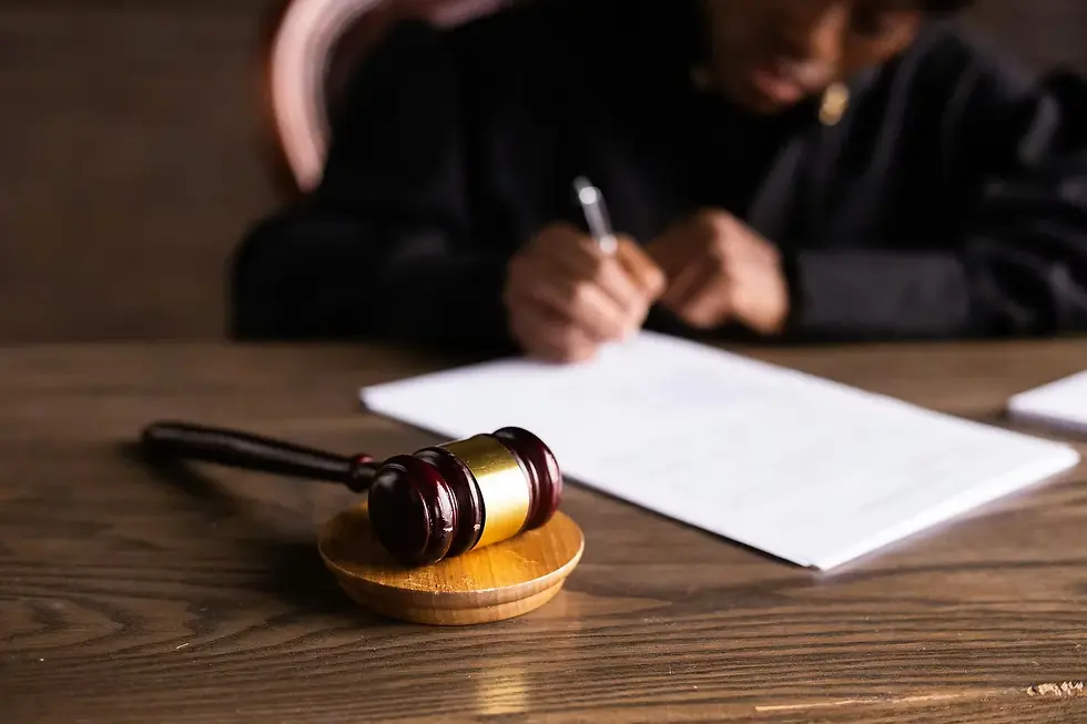 A judge writes at a wooden desk with a gavel in focus. The scene is serious, with a blurred background and a sense of authority.