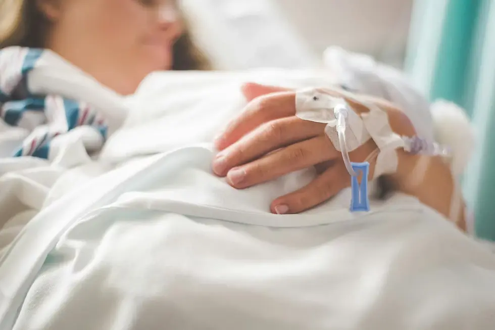 Person resting in a hospital bed, hand with an IV drip. Soft, warm light and white bedding create a peaceful atmosphere.