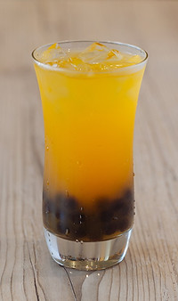 A refreshing glass of mango green tea garnished with fresh boba, showcasing vibrant colors and a fun beverage choice.
