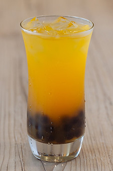 A refreshing glass of mango green tea garnished with fresh boba, showcasing vibrant colors and a fun beverage choice.
