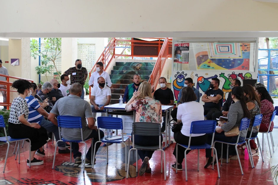 Grupo de cerca de 20 pessoas discute sobre sua regional. Sentados em círculo, há um mesa no centro com mapas.