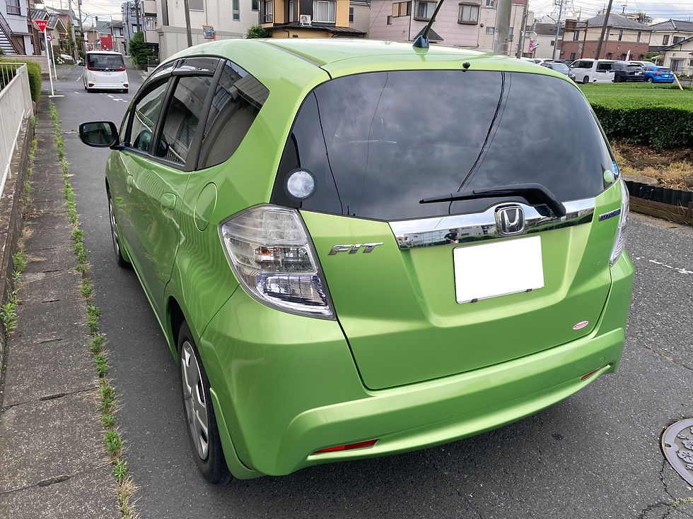 住宅街の路上に停車した黄緑のホンダ・フィットハイブリッドの後ろ姿。FIT HYBRIDとHondaエンブレムが見え、曇り空が窓に映る。