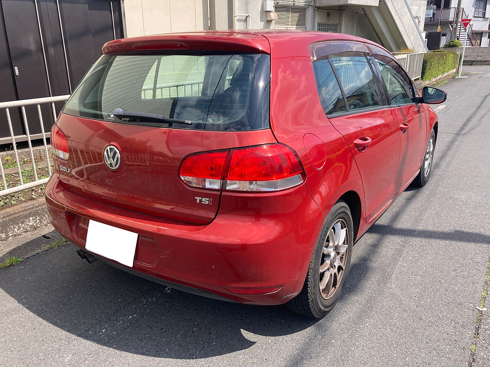 赤いフォルクスワーゲン・ゴルフのリアビュー。晴れた日に住宅街の道に駐車。ナンバープレートは白く塗りつぶされている。