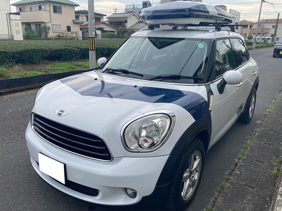 住宅街の道路に停まる白と紺のMINI クロスオーバー。ルーフボックスを載せ、前面にMINIロゴが見える。
