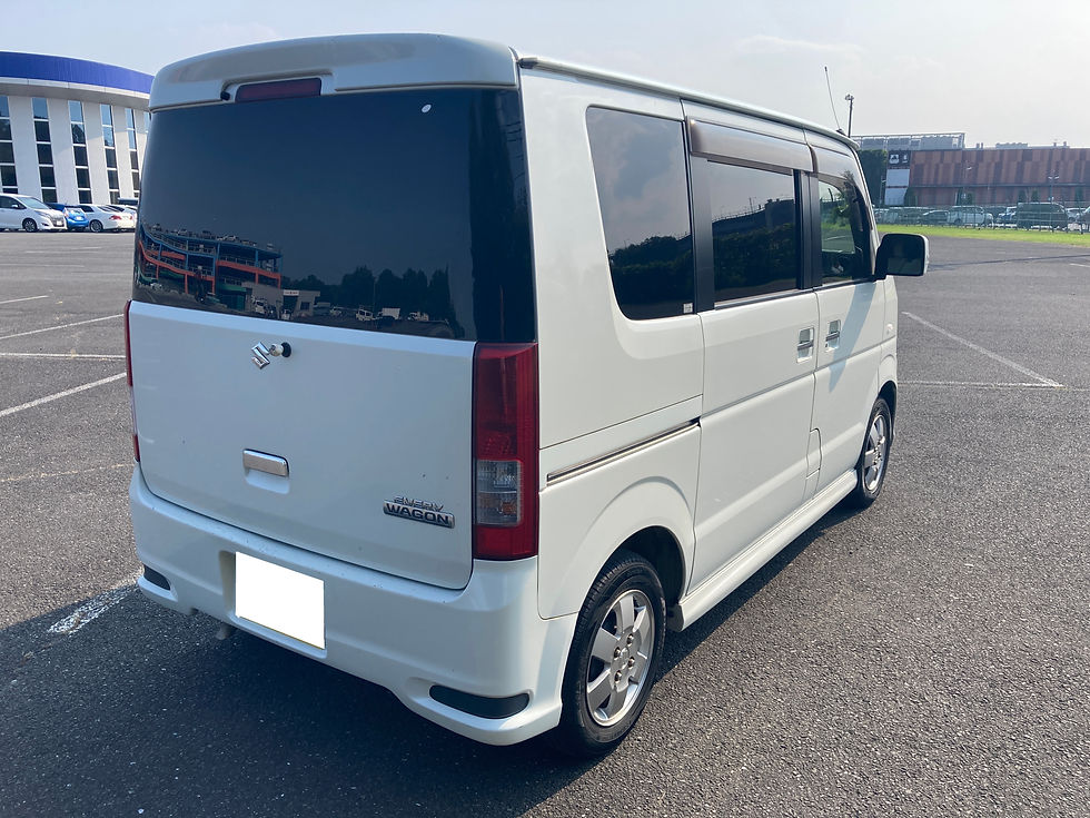 駐車場に停まる白いスズキのエブリイワゴン。後方から見た車体で、黒いスモーク窓と晴天の空が映る。