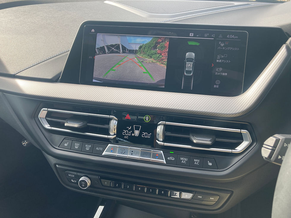 車内のダッシュボード中央画面に、バックカメラ映像と緑・赤の駐車ガイド線、右側に日本語の駐車支援メニューが表示されている