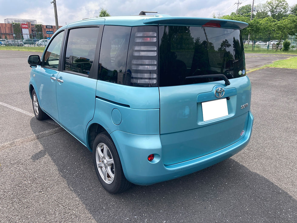 青いシエンタが駐車場に停められている。トヨタのロゴが後部に見える。背景に緑の木々と建物がある。晴れた日。