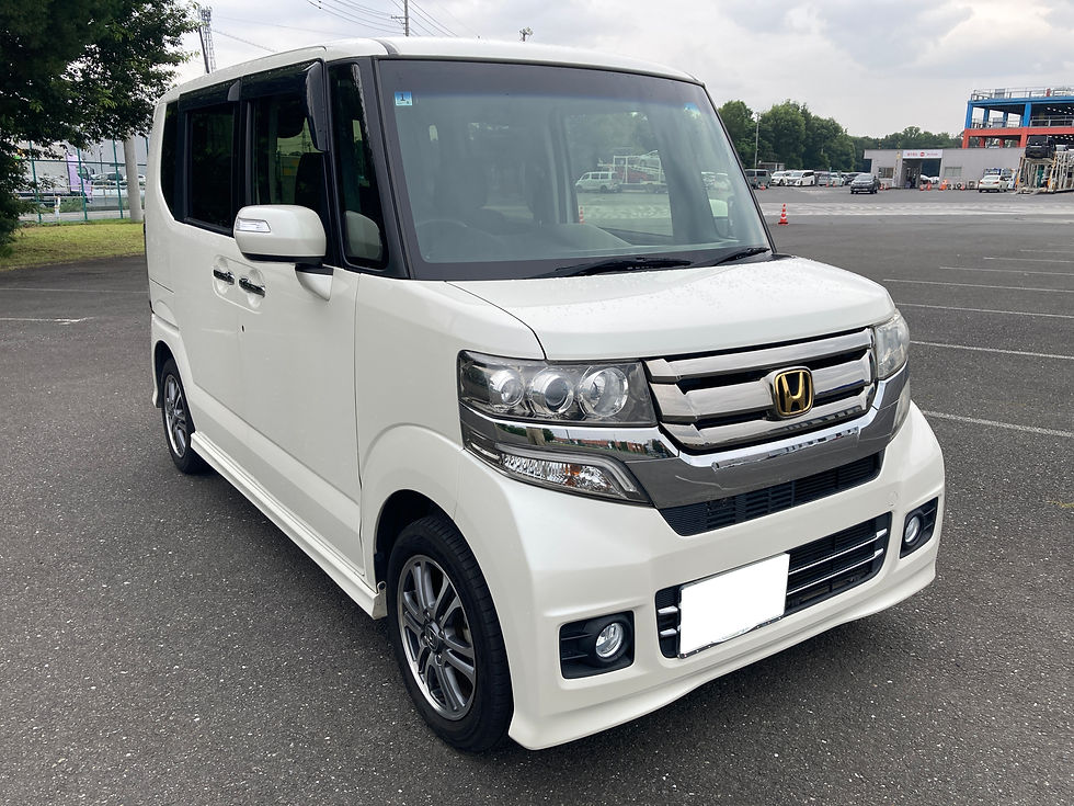 白いホンダのN-BOXが駐車場に停車している。フロントのメッキグリルと黒い窓が目立ち、曇り空の下で静かな雰囲気。