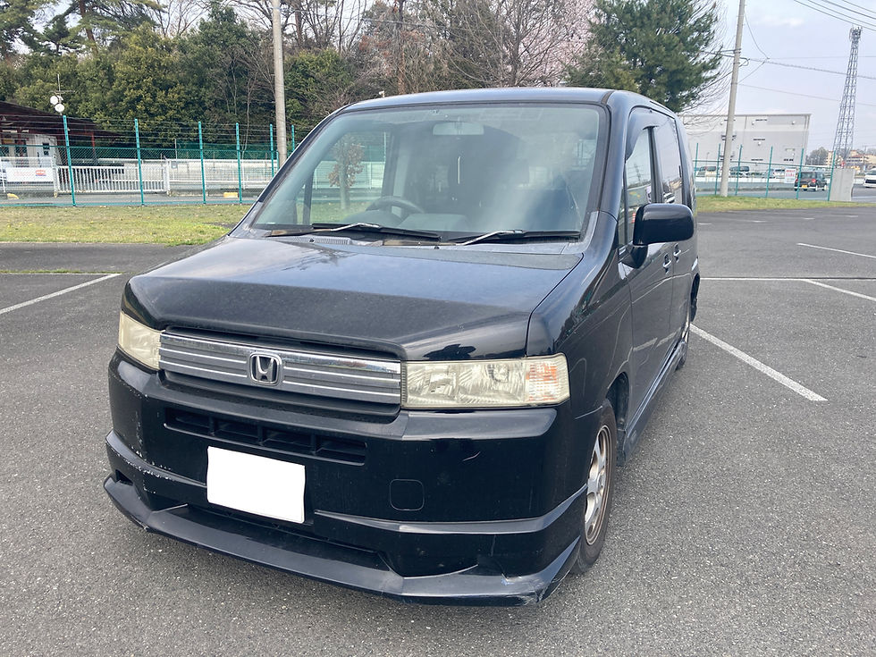 黒いモビリオスパイクが駐車場に停車。背景に緑のフェンスと木々が見える曇りの日。静かな雰囲気が漂う。