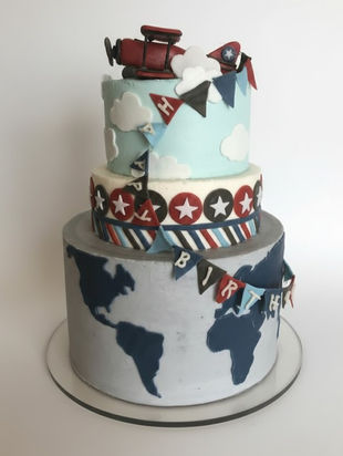 Three-tier world-map themed cake with fondant travel decorations and airplane details.