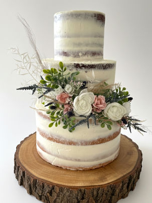 Semi-naked wedding cake with greenery and pastel flowers on a wood slice stand.