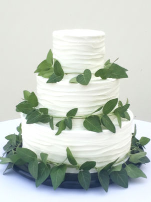 White three-tier wedding cake decorated with cascading green ivy leaves.