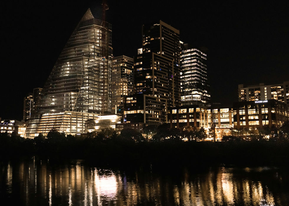 Night view of illuminated city skyscrapers reflecting on a river. Prominent glass building with triangle top, dark sky, urban scene. Austin, Texas