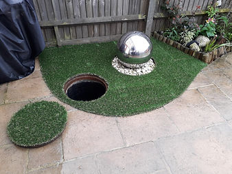 artificial grass around a water feature and camouflaging an inspection cover