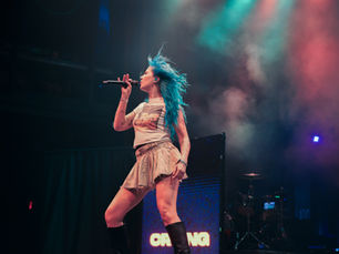 Charlotte Sands performing at Summer School Fest in Silver Spring, vocalist with bright teal hair singing into a microphone on stage under teal and pink stage lighting