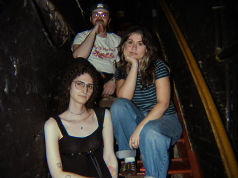 Mer Marcum photographed backstage at Mercury Lounge in New York City, three band members posing on a staircase in a dark backstage area