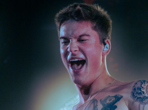Cameron Whitcomb performing at The Music Box in San Diego, shirtless vocalist with chest tattoos singing with intense expression under warm stage lighting