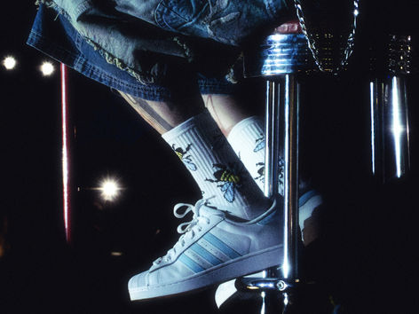 Close-up of Machine Gun Kelly's white Adidas Superstar sneakers and ripped denim shorts mid-air on stage at PNC Bank Arts Center, captured by photographer Stephanie Axelrod.