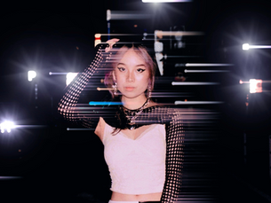 Amelie Jat in a white crop top and black mesh sleeves posing against a dramatic dark backdrop with streaking stage lights in a glitchy, cinematic double-exposure portrait.
