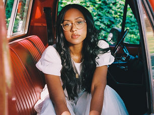 Artist, Jensen McRae, in a car looking at the camera in a white dress