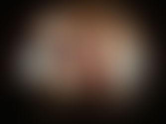 Lora Mouna and bandmates posing backstage at Mercury Lounge in New York City, four band members mugging for the camera against an exposed brick wall shot with a fisheye lensphed backstage at Elsewhere in Brooklyn, wearing a red lace top and black dress with dramatic makeup and Vivienne Westwood earrings against a warm orange wall