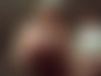 Loulia performs on stage in a deep red dress, holding a microphone and looking down with a soft smile, while a drummer plays behind her under warm stage lighting.