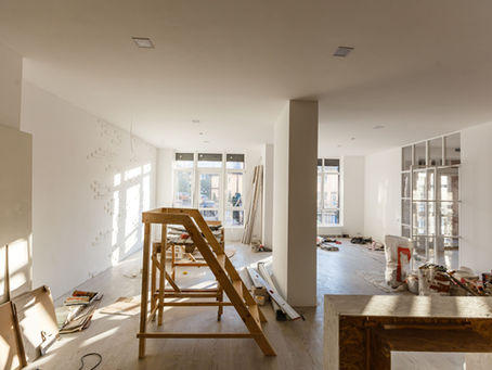 Sunlit room under renovation, with wooden scaffolding, scattered tools, and materials. White walls, large windows, and a calm, productive vibe.