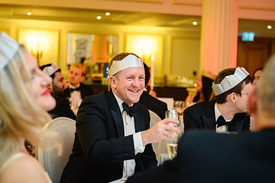 Guests in black tie and paper crowns laughing over Christmas dinner at the Linklaters party