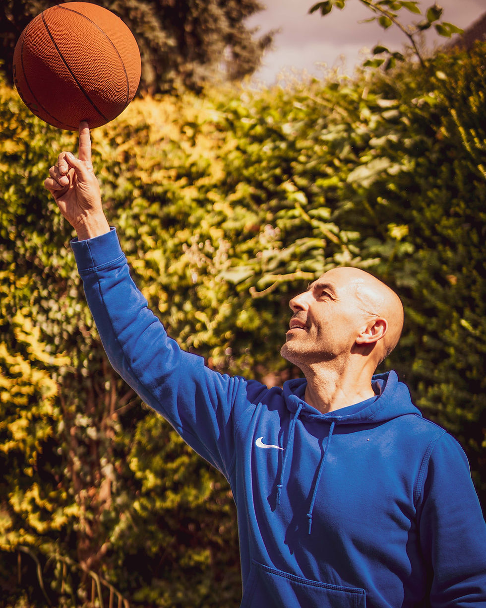 Mentalcoach Ilias Moschos im blauen Hoodie lächelt und balanciert einen Basketball auf dem Zeigefinger