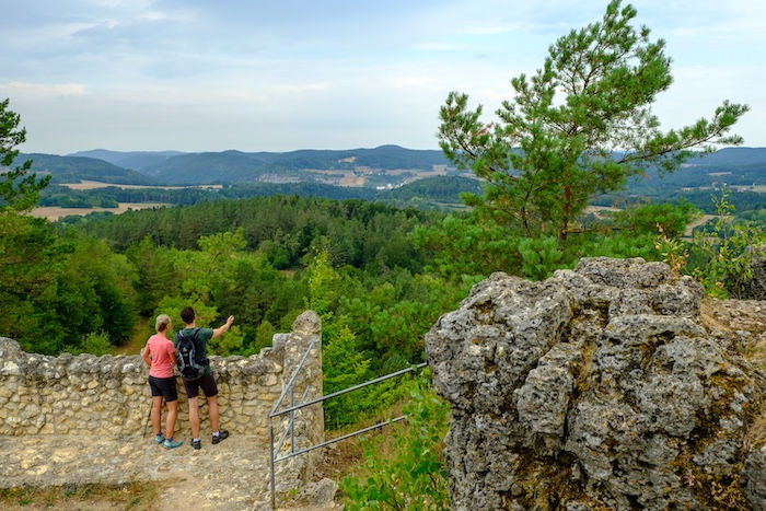 Paar auf Ruinenmauer blickt auf Tal, Felsbrocken mit Kiefer vorne