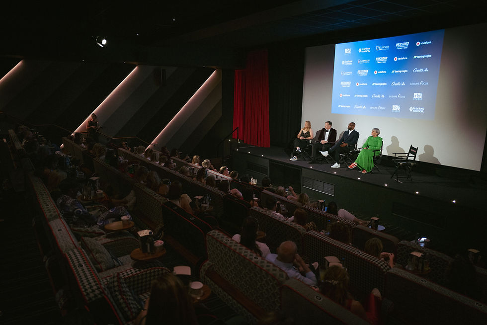 A packed cinema ask questions to 4 members of a panel on a stage in front of a cinema screen