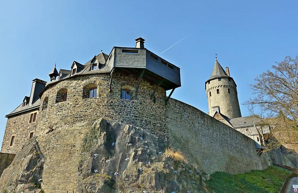 Stone castle with turrets set on a rocky hill under a clear blue sky. The castle has textured brick walls and a steep, grassy incline.