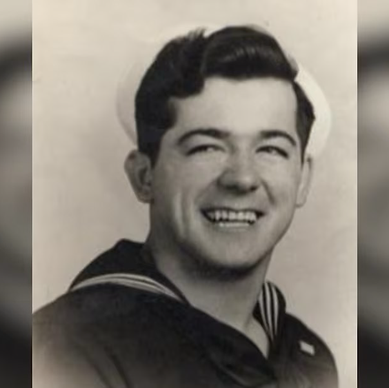 A black and white photo of Mickey Ganitch, a Caucasian male, clean shaven, with dark hair  in a sailor uniform with a white sailor hat.