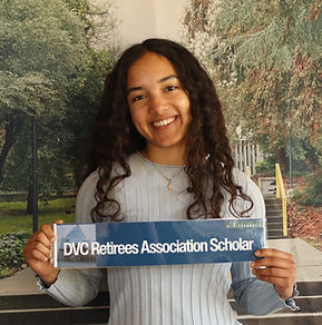A woman with curly, dark brown hair in a light blue shirt holding a DVC Retirees Association sign.