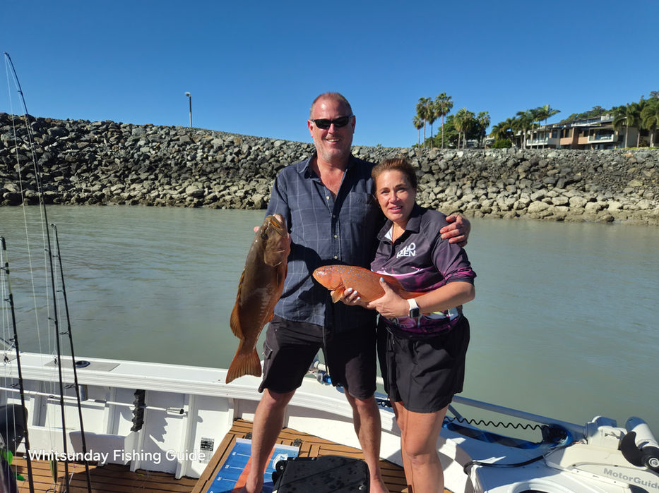 Two guests holding coral trout aboard a Whitsundays fishing charter boat
