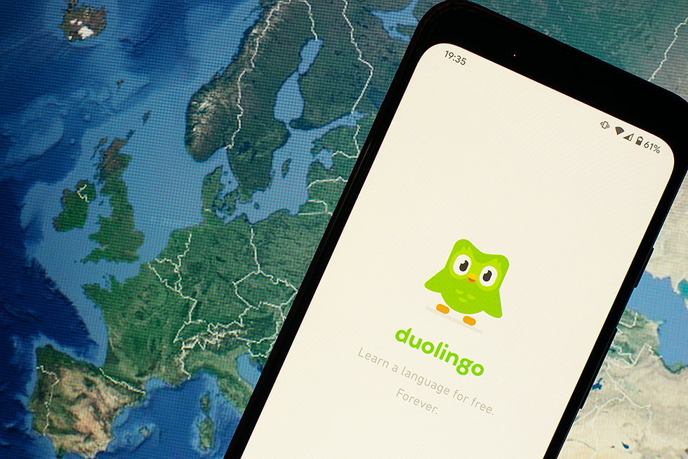 A phone with the Duolingo app opened in front of a map of Europe