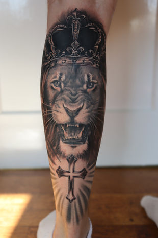 A black and grey tattoo of a lion with a crown on a leg. Made in Llangefni, Isle of Anglesey, North Wales by Shelley Williams. 
