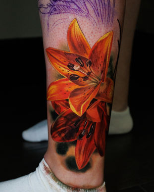 Colour tattoo of an orange lilies on a leg. It's a cover up of an older tattoo. Made in Llangefni, Isle of Anglesey, North Wales by Shelley Williams.