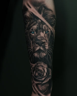 A black and grey tattoo of a lion with blue eyes on an arm. Made in Llangefni, Isle of Anglesey, North Wales by Shelley Williams. 