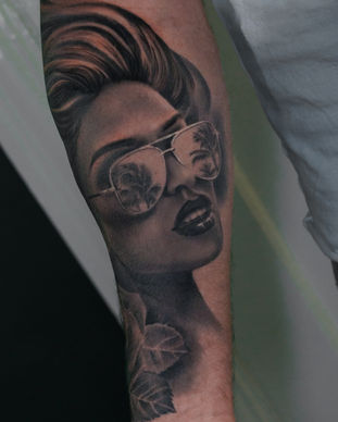 A black and grey portrait tattoo of a pin up lady wearing sunglasses on an arm. Made in Llangefni, Isle of Anglesey, North Wales by Shelley Williams.