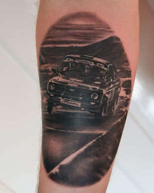 A black and grey tattoo of a rally car on an arm. Made in Llangefni, Isle of Anglesey, North Wales by Shelley Williams. 