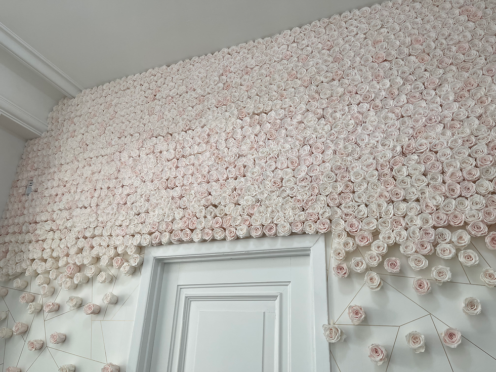 Wall covered in pale pink and white paper roses above a white door, creating a soft, romantic floral backdrop