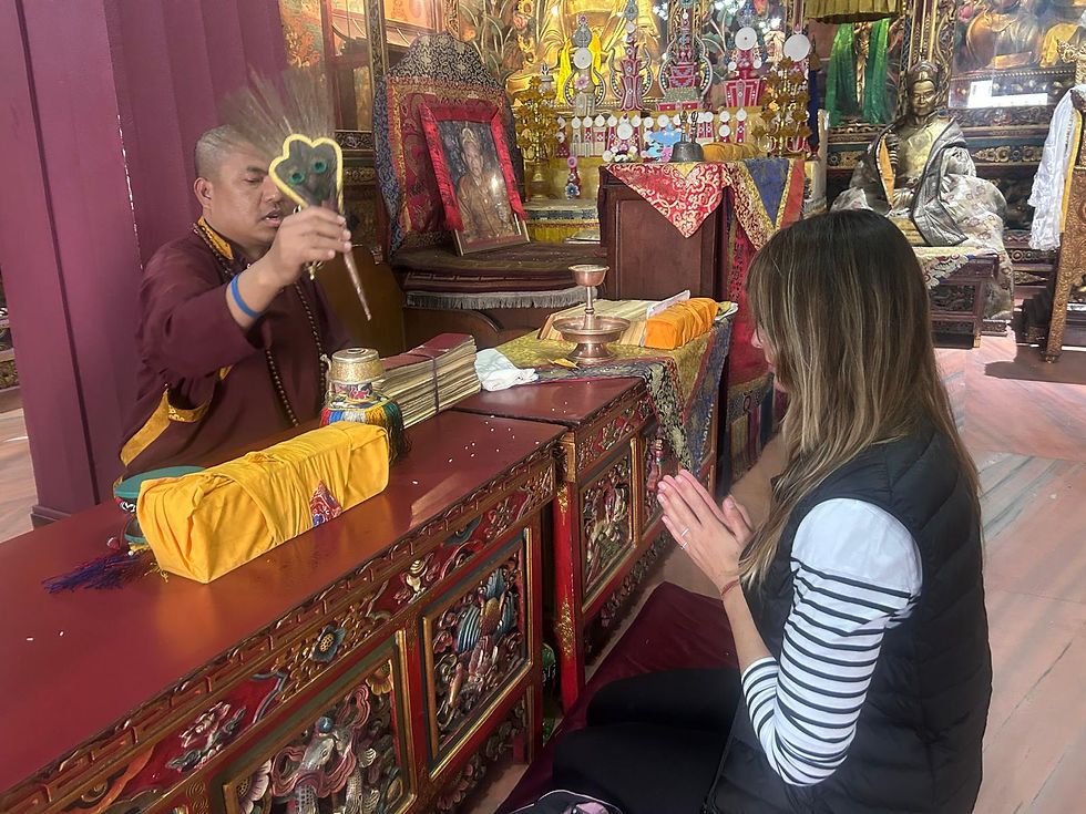 Monk blesses kneeling woman with a ritual fan in a colorful Buddhist temple filled with gold statues and offerings